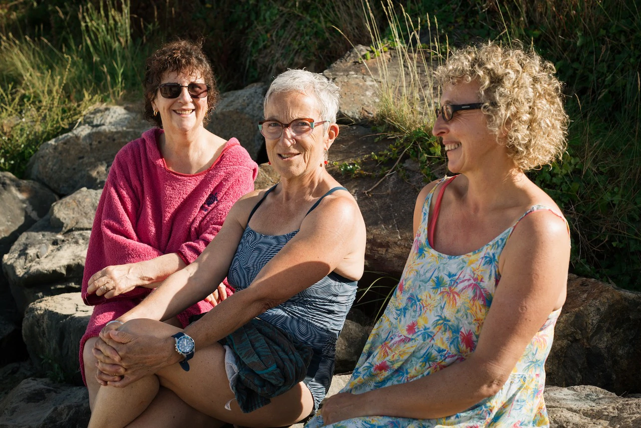 Trois femmes, la cinquantaines, assises sur la plage au soleil après leur session de longe-côte